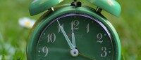 Grüner Retro-Wecker auf einer Wiese zeigt 11:55 Uhr